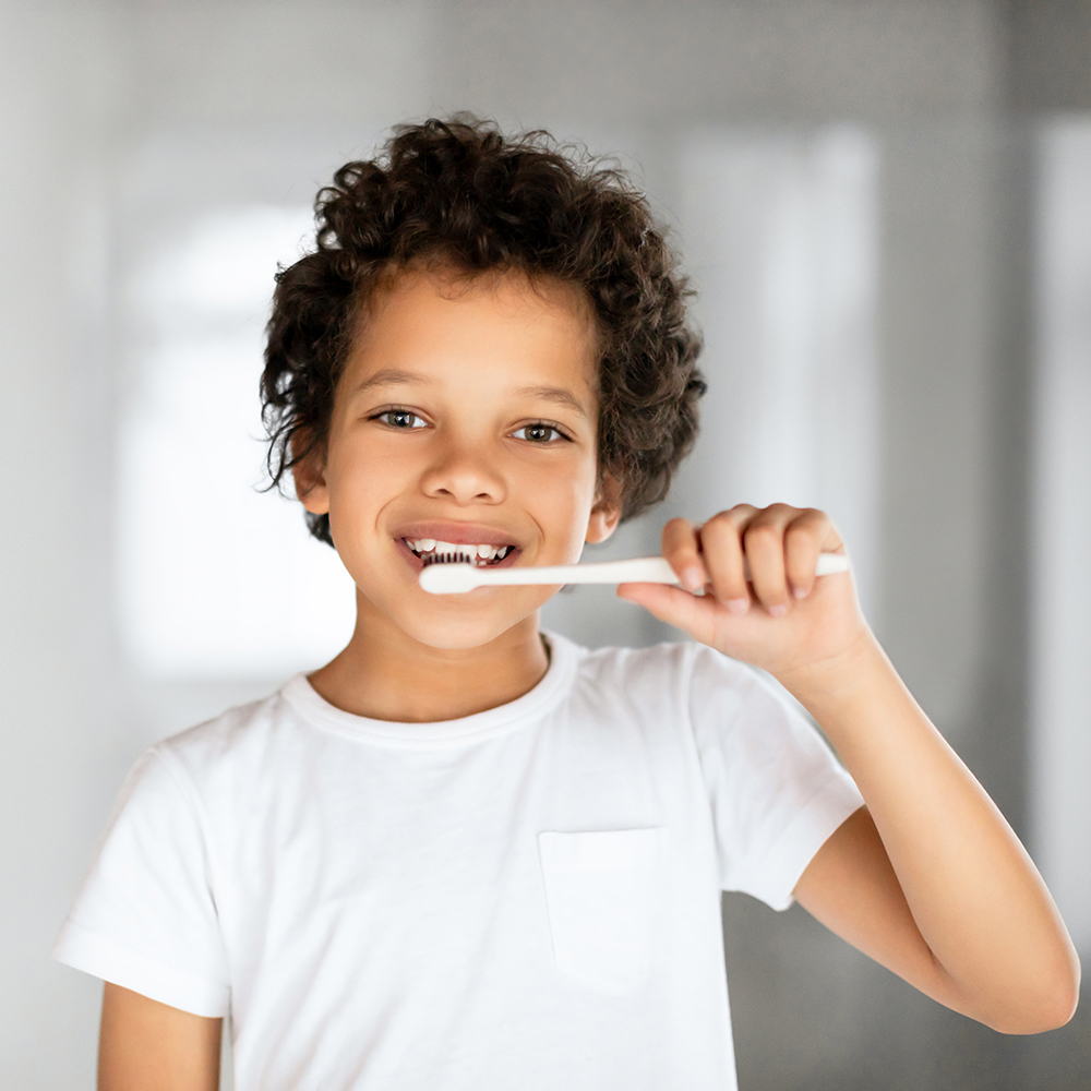 A smiling African American child with curly hair enjoys brushing their teeth in a clean, well-lit bathroom. This vibrant moment encourages good dental hygiene practices among young children.